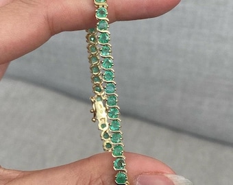 May include: A gold tennis bracelet with a row of round, green emeralds.