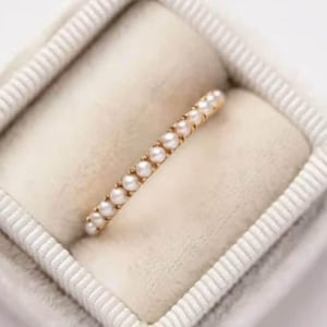 May include: A delicate gold band ring with a row of small white pearls.