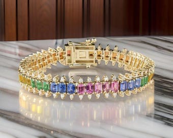 May include: A gold bracelet with a row of colorful gemstones, including yellow, green, blue, and pink. The bracelet is set with small diamonds along the edge.