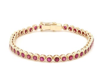 May include: A gold-colored bracelet featuring a series of round, vibrant red gemstones. The gemstones are set closely together, creating a continuous line of color. The bracelet has a secure clasp.