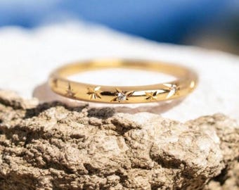 Puede incluir: Un fino anillo de banda de oro con una fila de pequeños diamantes engastados en forma de estrella alrededor de la banda.