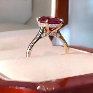 Könnte beinhalten: Ein Goldring mit einem großen, oval geschliffenen, tiefroten Edelstein in einer Krappenfassung. Die Galerie und die Ringschiene sind mit kleinen, klaren Diamanten im Pavé-Besatz verziert, die den Edelstein umranden und den Steg schmücken.