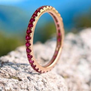 Pode incluir: Um delicado anel de banda de ouro com uma fileira de pequenas pedras de rubi vermelho brilhante engastadas em toda a banda.