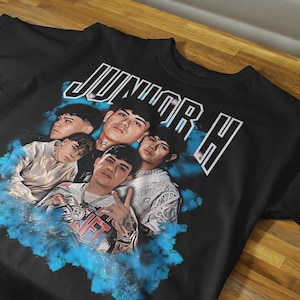 Pode incluir: Camiseta preta com uma estampa gráfica de quatro homens em um design de fumaça azul e branco. O texto "JUNIOR H" é impresso em branco na camiseta.