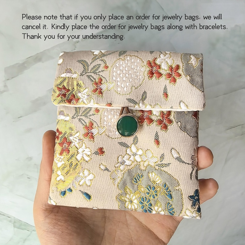 May include: A small square fabric pouch with a beige base featuring a woven floral pattern in red, white, and blue. The pouch has a flap closure secured by a round green button. Text above reads: Please note that if you only place an order for jewelry bags, we will cancel it. Kindly place the order for jewelry bags along with bracelets. Thank you for your understanding.