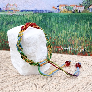 May include: A vibrant macrame bracelet featuring a mix of red, yellow, green, blue, and orange threads. The bracelet is presented on a white block, with a painting in the background. The text "Vincent van Gogh" is visible.
