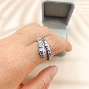 Op de afbeelding: Een zilveren slangenring met heldere zirkonia-stenen. De ring is om een vinger gewikkeld.