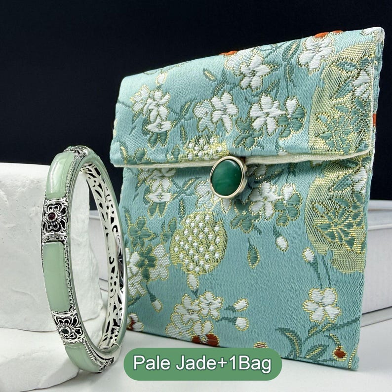 May include: A pale green jade bracelet with ornate silver detailing and a matching floral-patterned pouch. The pouch is teal with white and gold floral designs and a green stone clasp. The text "Pale Jade+1Bag" is at the bottom.
