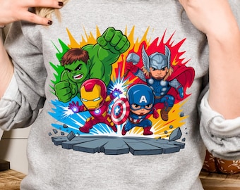 May include: A gray sweatshirt featuring a colorful graphic of four cartoon superheroes: Hulk, Iron Man, Captain America, and Thor. The superheroes are depicted with dynamic poses and surrounded by vibrant color bursts.