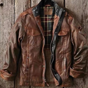May include: A brown leather jacket featuring a stand-up collar, a front zipper closure with a snap-button placket, two chest pockets with flaps, and long sleeves. The interior is lined with a black, red, and yellow plaid fabric pattern.