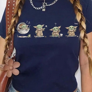 May include: Navy blue t-shirt featuring a graphic of a character from a popular science fiction series. The graphic shows the character in different poses. The shirt is a crew neck and has short sleeves.