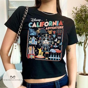 以下が含まれることがあります： ディズニー・カリフォルニア・アドベンチャーのテーマパークのカラフルなグラフィックが特徴の黒いTシャツ。ミッキーマウス、カーズのキャラクター、その他のパークのアイコンがデザインされています。「Disney California Adventure」の文字が上部に表示されています。