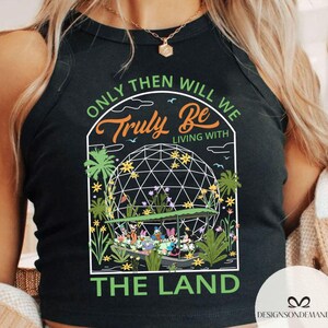 May include: Black tank top featuring a graphic of a geodesic dome with the text "ONLY THEN WILL WE TRULY BE LIVING WITH THE LAND." The graphic includes cartoon characters and floral elements.
