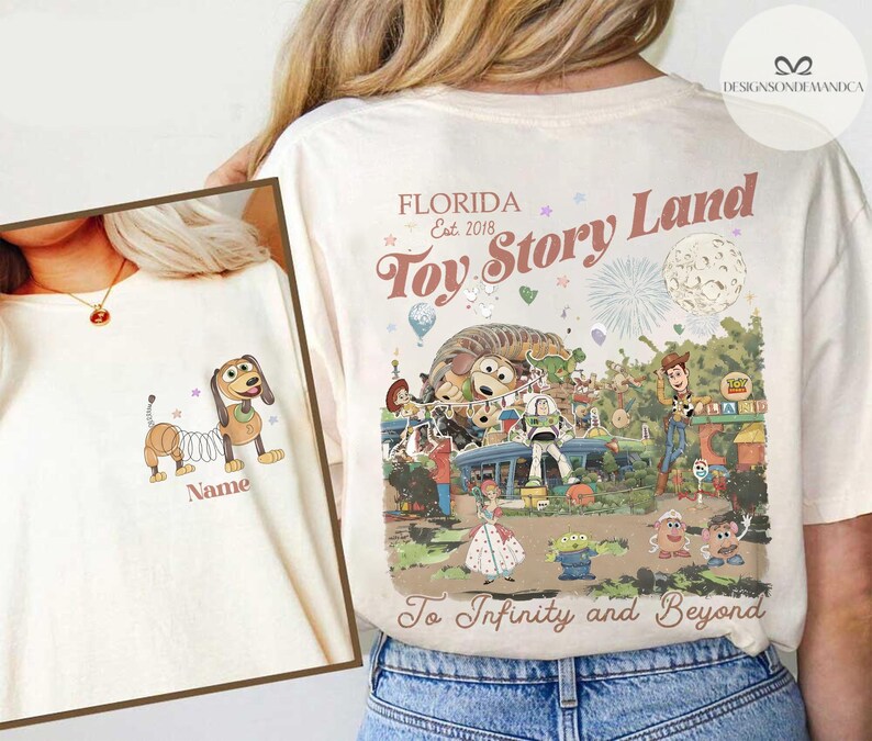 Puede incluir: Camiseta color crema con una ilustraci&oacute;n de dibujos animados de Slinky Dog y el texto "Name" en la parte delantera. La parte trasera de la camiseta muestra un gr&aacute;fico colorido de Toy Story Land en Florida, con el texto "Toy Story Land" y "To Infinity and Beyond".
