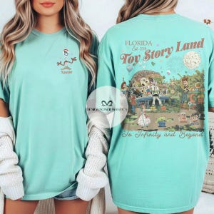 Puede incluir: Una camiseta de color verde azulado claro con un dise&ntilde;o de dibujos animados de Forky y la palabra "Name" debajo. La parte trasera de la camiseta muestra un colorido dise&ntilde;o de "Toy Story Land" con el texto "Florida Est. 2018" y "To Infinity and Beyond."