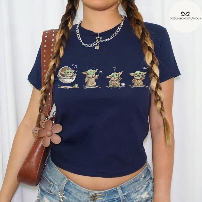 May include: Navy blue t-shirt featuring a graphic of a character from a popular science fiction series. The graphic shows the character in different poses. The shirt is a crew neck and has short sleeves.