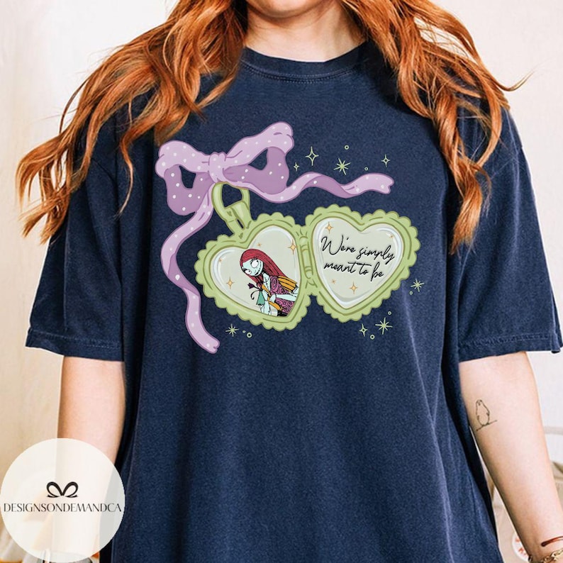 Puede incluir: Camiseta azul marino con un dise&ntilde;o de medall&oacute;n en forma de coraz&oacute;n con Sally de Pesadilla antes de Navidad. El medall&oacute;n tiene un borde verde claro y un lazo rosa. El texto "We're simply meant to be" tambi&eacute;n est&aacute; en la camiseta.