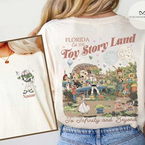 Puede incluir: Camiseta color crema con un gr&aacute;fico colorido de los personajes de Toy Story en Toy Story Land en Florida. La camiseta incluye el texto "Toy Story Land" y "To Infinity and Beyond."