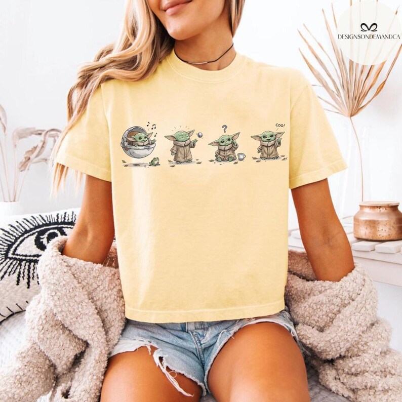May include: A light yellow t-shirt featuring a cartoon sequence of a character from a popular science fiction series. The character is depicted in various poses, including one with the word "Cool". The shirt is made of a soft material.