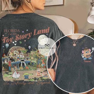 Puede incluir: Camiseta gris oscuro con un colorido gr&aacute;fico de Toy Story Land en la espalda con el texto "Florida Est. 2018" y "To Infinity and Beyond". La parte delantera tiene un gr&aacute;fico de Mr. Potato Head con el texto "Name".