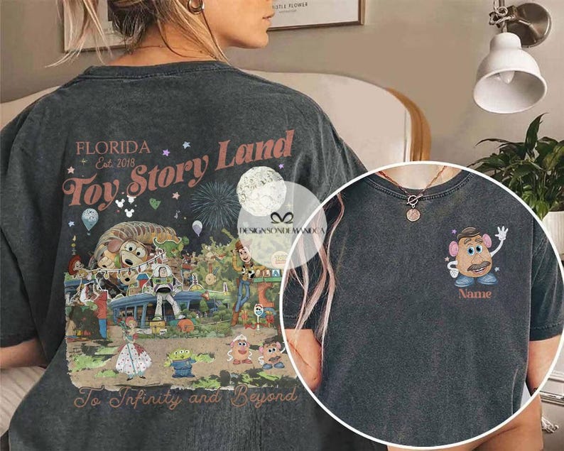Puede incluir: Camiseta gris oscuro con un colorido gr&aacute;fico de Toy Story Land en la espalda con el texto "Florida Est. 2018" y "To Infinity and Beyond". La parte delantera tiene un gr&aacute;fico de Mr. Potato Head con el texto "Name".