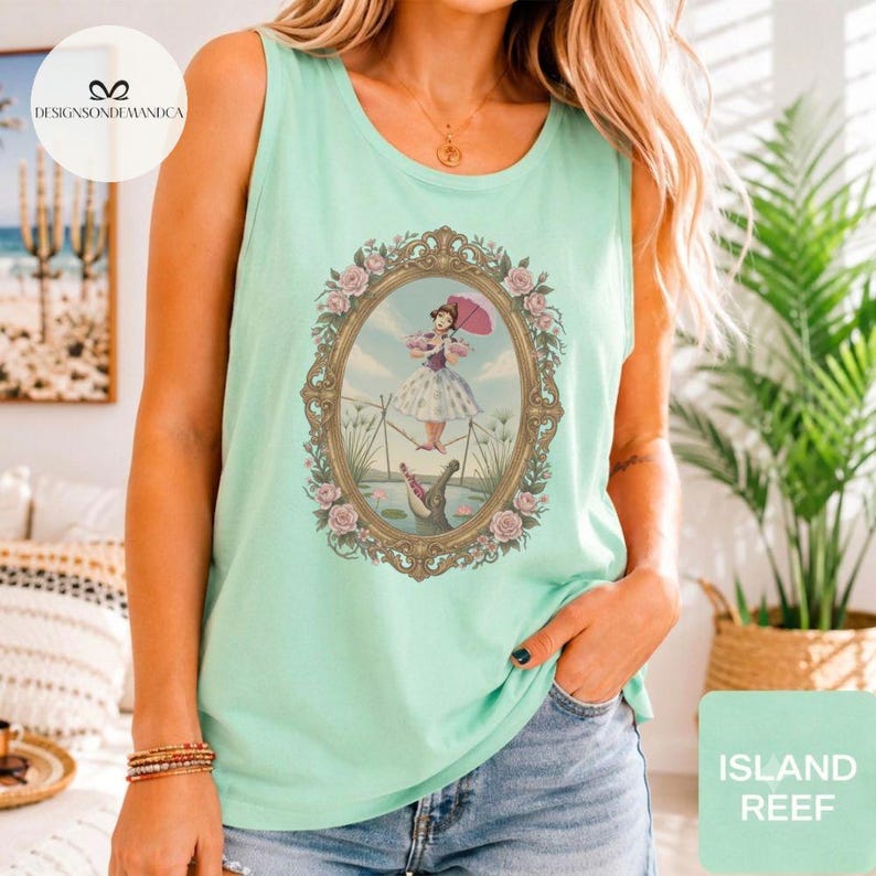 May include: A light mint green sleeveless tank top featuring a central graphic of a person in a dress holding a pink umbrella while balancing on a tightrope above an alligator, all enclosed within an ornate, rose-adorned oval frame.
