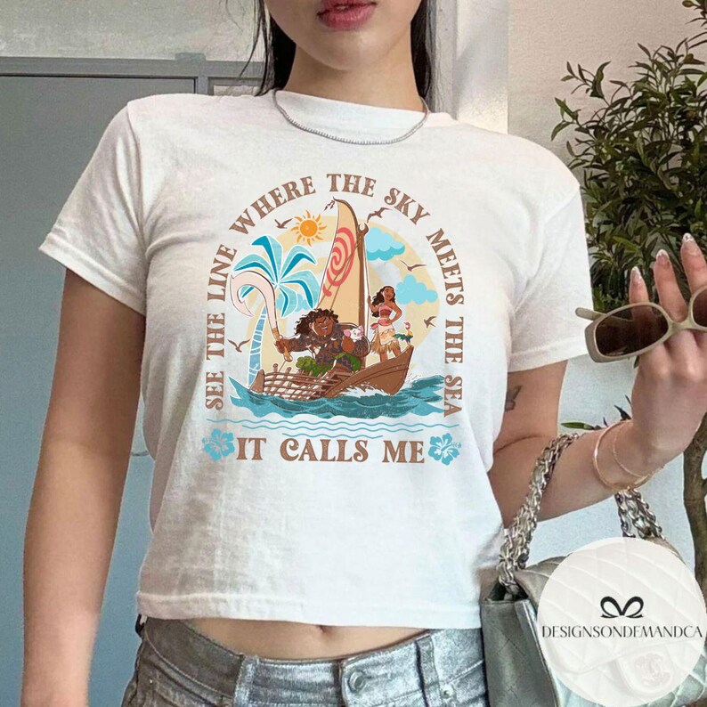 May include: White t-shirt featuring a colorful illustration of a boat with characters and the text "SEE THE LINE WHERE THE SKY MEETS THE SEA IT CALLS ME". The design includes a sun, palm trees, and ocean waves.