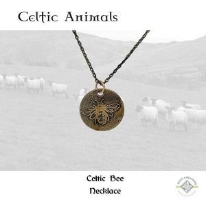 May include: A Celtic Bee necklace with a bronze pendant featuring a detailed bee design. The necklace is on a black chain and is photographed against a backdrop of a field with sheep.