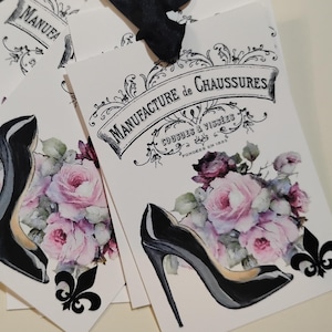 May include: White tags with a black high-heeled shoe illustration and a bouquet of pink and purple roses. The tags have the text "Manufacture de Chaussures" in a decorative banner.