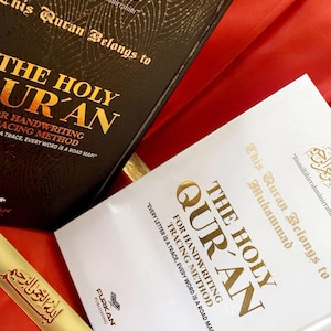 Può includere: Due copie del libro "The Holy Qur'an" con scritte dorate e un segnalibro dorato. Un libro è nero, l'altro è bianco. Il testo include "For Handwriting Tracing Method" e "Every Letter is a Trace, Every Word is a Road Map!"