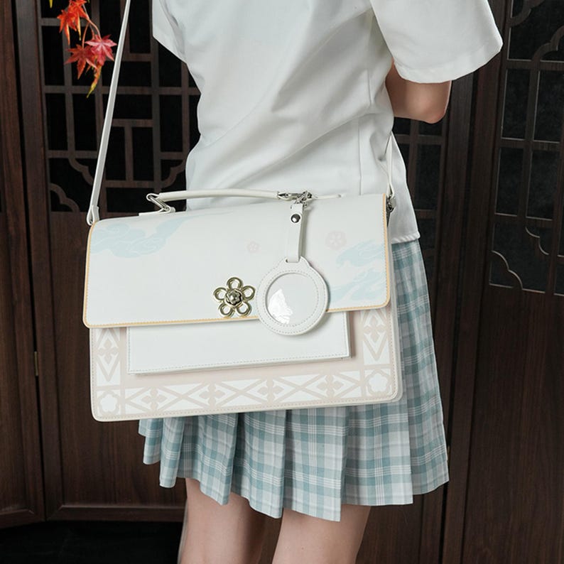 Pu&ograve; includere: Una borsa a tracolla bianca e rosa con un motivo floreale e un ciondolo circolare trasparente. La borsa ha una tracolla lunga e un manico superiore.