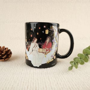 May include: Black ceramic mug with a white crescent moon design. The moon features two figures in traditional Chinese clothing, surrounded by lanterns and stars. The mug has a black handle and the text "Global" on the bottom.