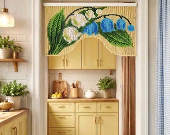 May include: A beaded doorway curtain featuring a floral pattern of white lily of the valley flowers, blue bell-shaped blossoms, and green leaves against a light yellow background, suspended from a white horizontal rod in a kitchen doorway.