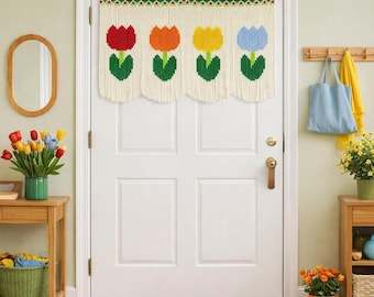 May include: A white door with a decorative valance featuring four colorful tulip designs. The tulips are red, orange, yellow, and blue, with green leaves. The valance hangs above a door with a brass doorknob. An orange doormat is on the floor.