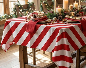 May include: A festive dining table set for a holiday celebration. The table is covered with a red and white striped tablecloth. The table is set with gold-rimmed plates, red napkins, and lit candles. Pinecones and greenery add to the holiday theme.