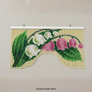 Puede incluir: Un tapiz de pared con cuentas que presenta un dise&ntilde;o floral de flores blancas y rosas con hojas verdes. La cortina de cuentas tiene un fondo color crema y est&aacute; montada en una barra blanca. El texto "PAFULIM HOME DECO" est&aacute; en la parte inferior.