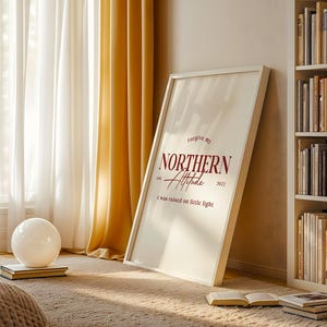 Framed typography print leaning against a wall near a window with curtains, books, and natural light.