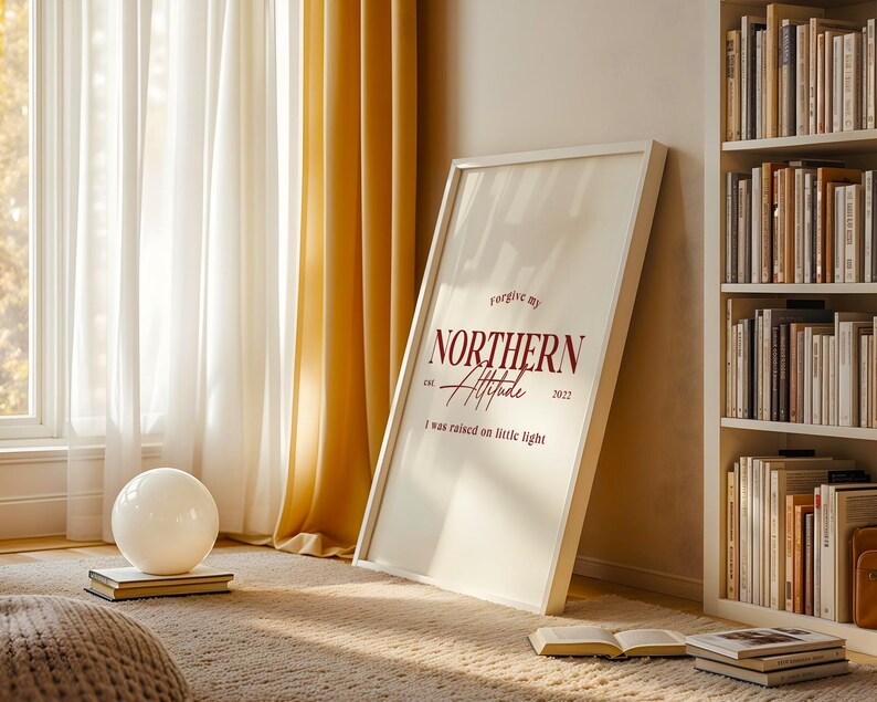 Framed typography print leaning against a wall near a window with curtains, books, and natural light.