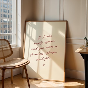 Può includere: Una stampa artistica incorniciata con la citazione "If I was empty space and you were a formless shape we'd fit" in scrittura bordeaux. Una sedia e un tavolo di legno sono nella stanza, con una finestra sullo sfondo.