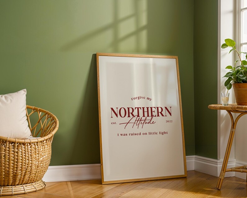 Framed typography print leaning against a green wall next to a woven basket and a plant on a light wood floor.