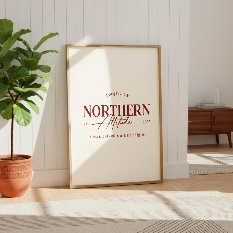 Framed typography print leaning against a white paneled wall next to a potted plant and a wooden bench.