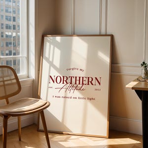 Framed typography print leaning against a wall in a workspace setting with a chair, desk, and window view.