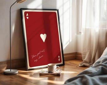 May include: A framed red playing card art print featuring the Ace of Hearts. The print has a white heart symbol and the text "You got all my love" in cursive. A coffee cup and a book are in front of the print.