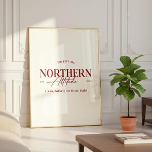 Framed typography print leaning against a white wall in a bright room with decorative molding and indoor plants.