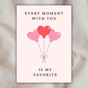 Pode incluir: Um cartão branco com o texto "Cada momento com você é o meu favorito" e três balões em forma de coração, dois rosa e um vermelho.