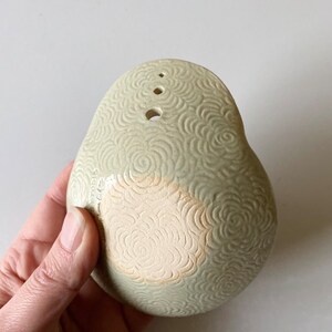 May include: A light green ceramic bowl with a textured floral pattern. The bowl has four small holes on the top and a larger hole on the bottom.