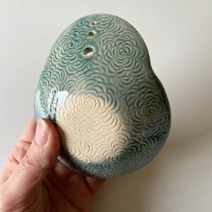 May include: A light blue ceramic planter with a white floral design. The planter has three drainage holes and a rounded shape.