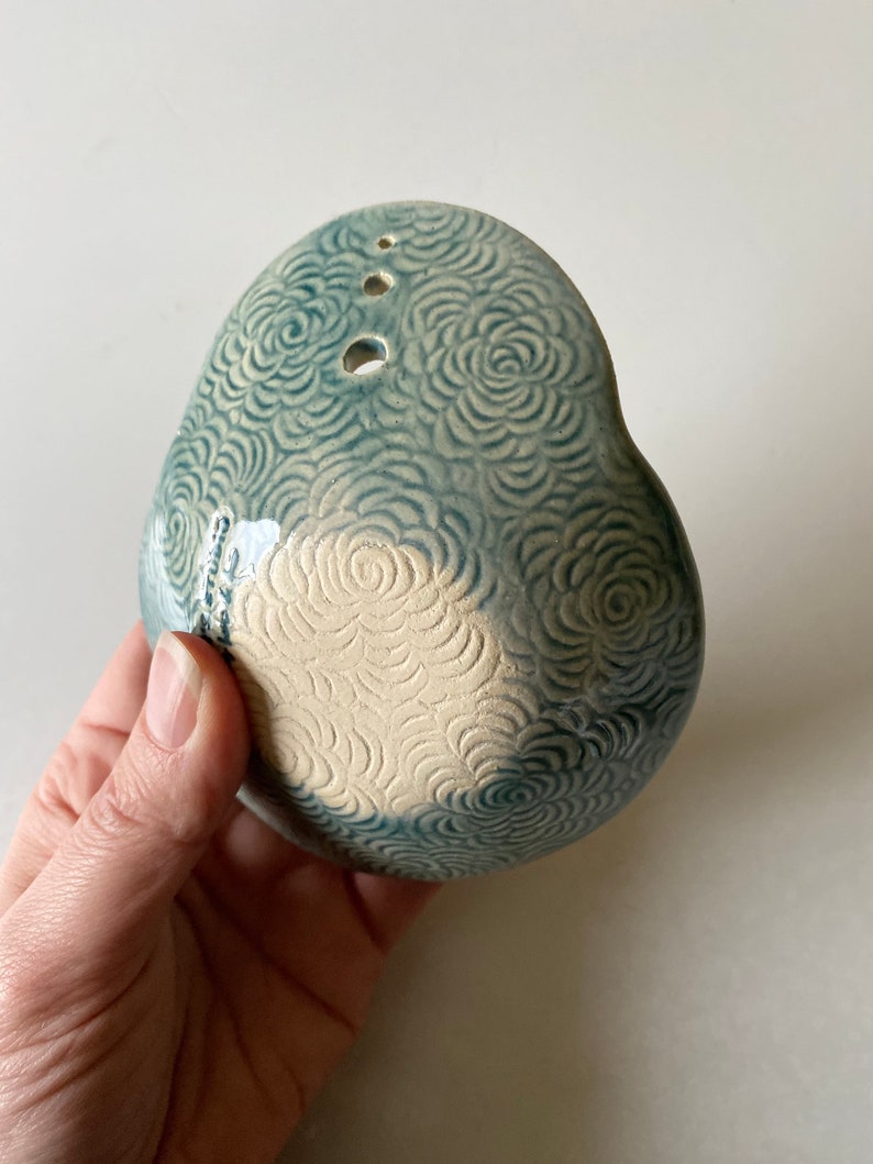 May include: A light blue ceramic planter with a white floral design. The planter has three drainage holes and a rounded shape.