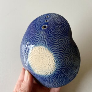 May include: A blue ceramic heart-shaped dish with a white center and a swirl pattern. The dish has several small holes in the top.