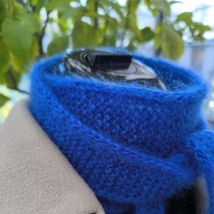 Op de afbeelding: Een felblauwe, pluche gebreide sjaal. De sjaal is gevouwen en gedrapeerd over een witte jas.